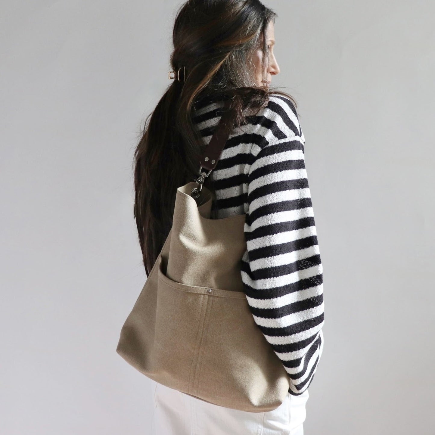 Lifestyle photo of model in white pants and black and white striped sweater holding casual canvas shoulder bag