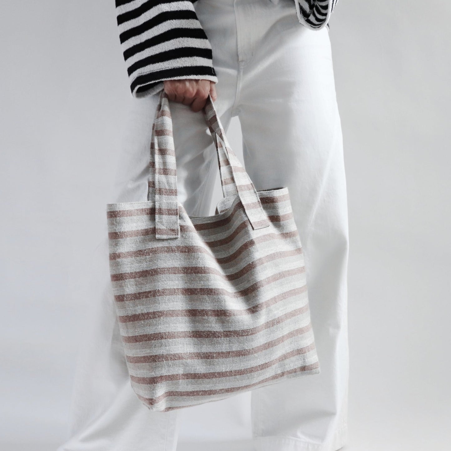 Striped Tote Bag in neutral color woven linen held by model in wide leg white pants